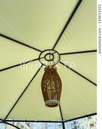 Light fixture hangs from the center of a large outdoor umbrella on a sunny day in a city, providing illumination for people below Light fixture hangs from the center of a large outdoor umbrella on a sunny day in a city, providing illumination for people below 140651022