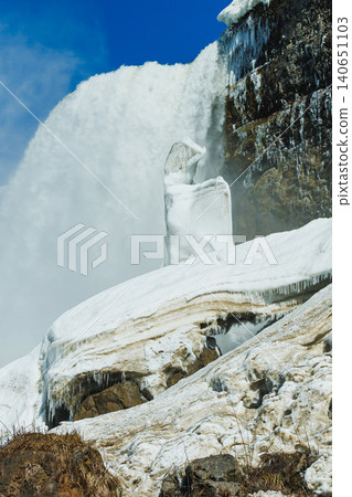 Niagara Falls shows ice and water flowing down during winter with frozen formations around the rocks and mist in the air from the falling water Niagara Falls shows ice and water flowing down during winter with frozen formations around the rocks and mist in the air from the falling water 140651103