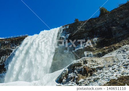 Niagara Falls shows water rushing down frozen rocks with clear sky overhead during winter season Niagara Falls shows water rushing down frozen rocks with clear sky overhead during winter season 140651110