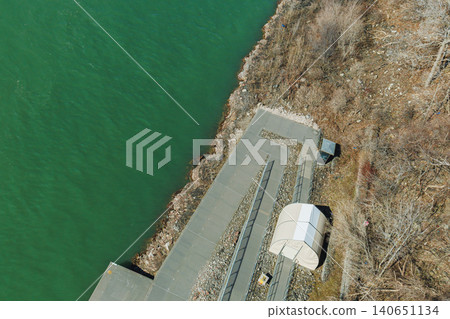 Dock area along a green river with a small shelter and rocky shore during a sunny day in early spring Dock area along a green river with a small shelter and rocky shore during a sunny day in early spring 140651134