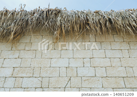 Sundrenched thatch atop stone wall. Cozy countryside setting with warm and cool shades. Idyllic seaside cottage exterior blending natural materials and tranquil ambiance Sundrenched thatch atop stone wall. Cozy countryside setting with warm and cool shades. Idyllic seaside cottage exterior blending natural materials and tranquil ambiance 140651209