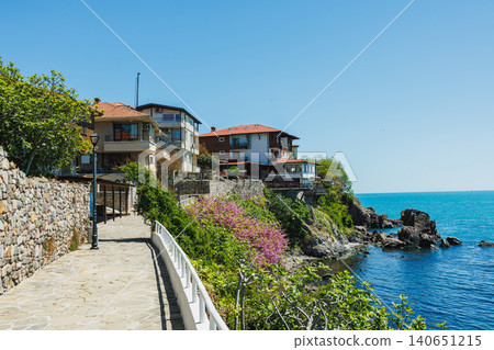 Sunny seaside stroll. Coastal path with scenic views. Serene seaside walkway overlooking rocky cliffs. Bright coastal trail alongside vibrant bougainvillea and calm waters Sunny seaside stroll. Coastal path with scenic views. Serene seaside walkway overlooking rocky cliffs. Bright coastal trail alongside vibrant bougainvillea and calm waters 140651215