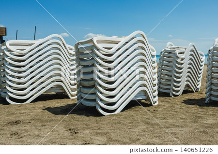 Calm seaside with colorful sky. Minimalist seaside landscape featuring flowing chair arrangements and vibrant sky with abstract white chairs stacked on sandy shore Calm seaside with colorful sky. Minimalist seaside landscape featuring flowing chair arrangements and vibrant sky with abstract white chairs stacked on sandy shore 140651226