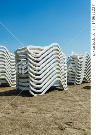 Detailed view of seaside lounge chairs. Close examination of poolside loungers in sunlight. Intimate shot capturing stacked lounge chairs and their shadows on sandy surface Detailed view of seaside lounge chairs. Close examination of poolside loungers in sunlight. Intimate shot capturing stacked lounge chairs and their shadows on sandy surface 140651227