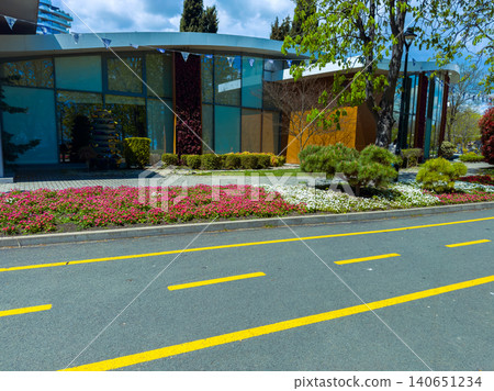 Flowers line the pathway beside a modern building in a city with trees and blue skies during daytime Flowers line the pathway beside a modern building in a city with trees and blue skies during daytime 140651234