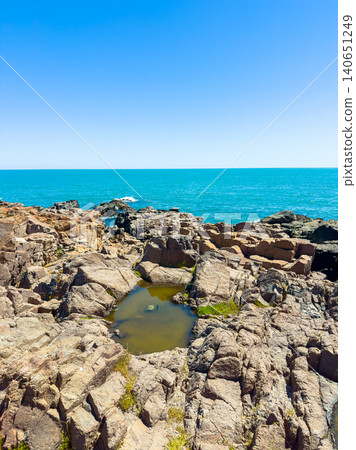 Rocky coastline near ocean with pools of water under a clear blue sky during daytime in a coastal location Rocky coastline near ocean with pools of water under a clear blue sky during daytime in a coastal location 140651249