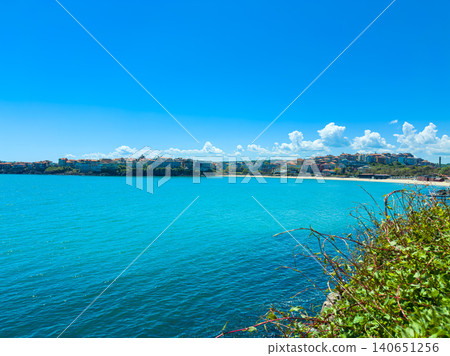Bright day at the coastal town with clear water and distant hills showcasing buildings along the shore Bright day at the coastal town with clear water and distant hills showcasing buildings along the shore 140651256