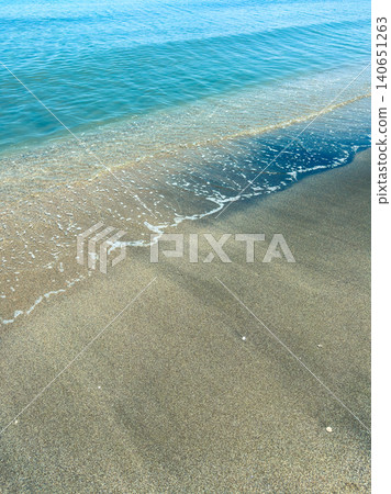 Waves gently wash over the sandy shore at a beach on a sunny day Waves gently wash over the sandy shore at a beach on a sunny day 140651263