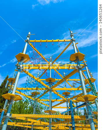 Climbing structure at an outdoor park with bright yellow equipment under a clear blue sky during a sunny day Climbing structure at an outdoor park with bright yellow equipment under a clear blue sky during a sunny day 140651264