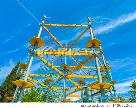 Children play on a tall climbing structure with ropes and yellow platforms during a sunny day at a park Children play on a tall climbing structure with ropes and yellow platforms during a sunny day at a park 140651265