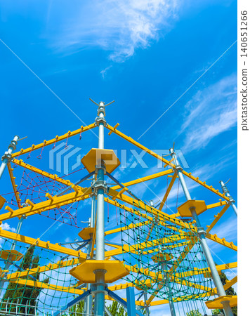 Bright day at a large climbing structure in a park where children play and explore while a few clouds float in the clear sky Bright day at a large climbing structure in a park where children play and explore while a few clouds float in the clear sky 140651266