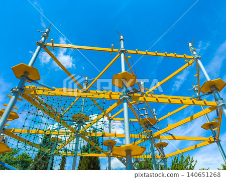 Bright yellow climbing structure stands under clear blue sky in a playground during daytime with sunlight shining on the ropes and framework Bright yellow climbing structure stands under clear blue sky in a playground during daytime with sunlight shining on the ropes and framework 140651268