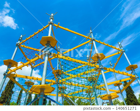 Bright climbing structure in a playground under a clear blue sky with some clouds during daytime 140651271