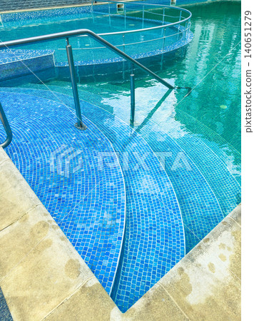 Water steps lead into a blue pool with a curved design in a recreational area during a sunny day 140651279