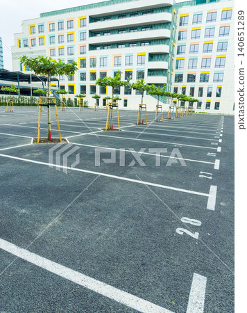 Parking lot area with newly planted trees near a modern building during the day in an urban setting Parking lot area with newly planted trees near a modern building during the day in an urban setting 140651289