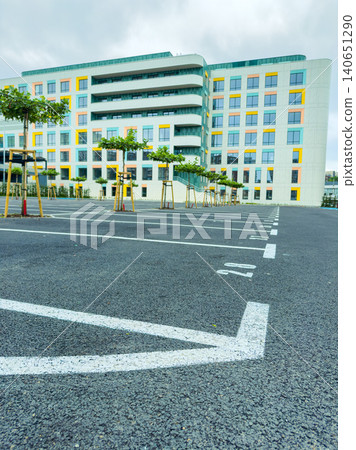 Parking lot next to a modern building with empty spaces and small trees on a cloudy day in the city Parking lot next to a modern building with empty spaces and small trees on a cloudy day in the city 140651290