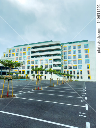 Building with parking spaces and trees located in an urban area under cloudy skies Building with parking spaces and trees located in an urban area under cloudy skies 140651291