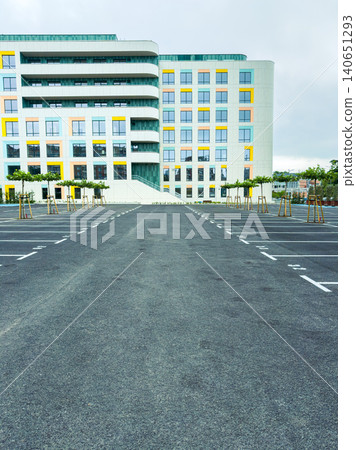Empty parking lot in front of a modern building during a cloudy day with few trees lined along the sides Empty parking lot in front of a modern building during a cloudy day with few trees lined along the sides 140651293