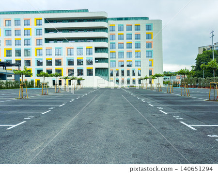 Empty parking lot in front of a multi-story building with colorful windows during cloudy weather in an urban area Empty parking lot in front of a multi-story building with colorful windows during cloudy weather in an urban area 140651294