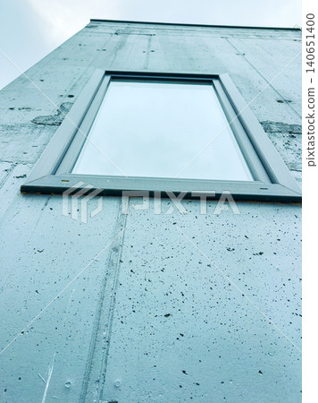 Building wall with a window looking up toward a gray sky in an urban area during the day Building wall with a window looking up toward a gray sky in an urban area during the day 140651400