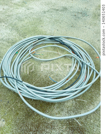 Several loops of gray conduit tubing are placed on a concrete surface in an outdoor area during a cloudy day Several loops of gray conduit tubing are placed on a concrete surface in an outdoor area during a cloudy day 140651403