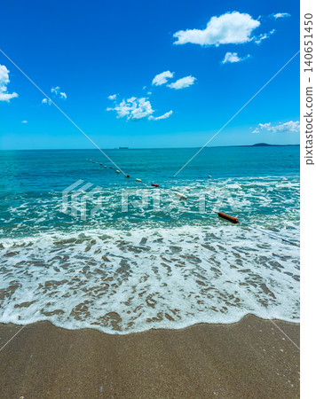 View of a beach with waves and a blue sky, showing a line of buoys marking a swimming area near water and shore during daytime View of a beach with waves and a blue sky, showing a line of buoys marking a swimming area near water and shore during daytime 140651450