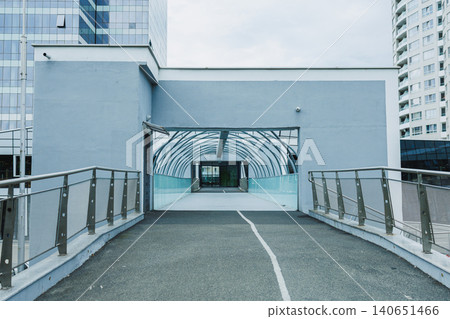 Modern walkway connects buildings in urban area, showcasing glass architecture and smooth pavement during cloudy day Modern walkway connects buildings in urban area, showcasing glass architecture and smooth pavement during cloudy day 140651466