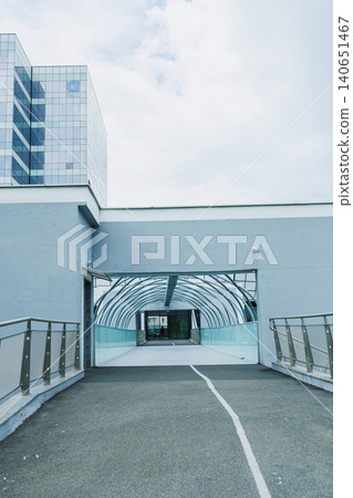 Walkway leads to a modern building with glass roof in an urban area during a cloudy day Walkway leads to a modern building with glass roof in an urban area during a cloudy day 140651467
