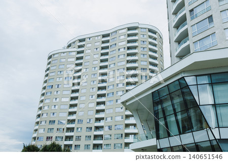 Many floors of a modern apartment building is seen from below against a cloudy sky in a city during daylight hours Many floors of a modern apartment building is seen from below against a cloudy sky in a city during daylight hours 140651546