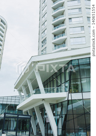 Modern building design features glass walls and sleek lines in an urban area with cloudy skies overhead in the early afternoon Modern building design features glass walls and sleek lines in an urban area with cloudy skies overhead in the early afternoon 140651554