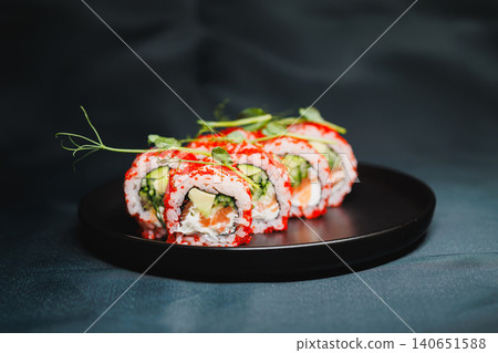 Sushi rolls with cucumber and crab on black plate served on dark background during dinner time Sushi rolls with cucumber and crab on black plate served on dark background during dinner time 140651588