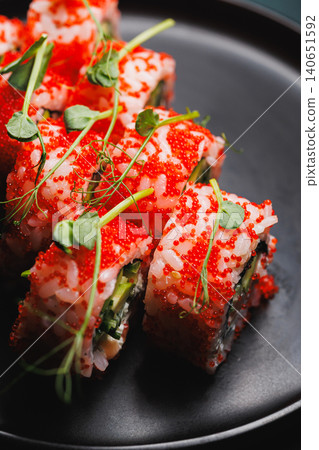 Sushi rolls made with fresh ingredients served on a black plate with bright red toppings and green accents at a restaurant during dinner time Sushi rolls made with fresh ingredients served on a black plate with bright red toppings and green accents at a restaurant during dinner time 140651592