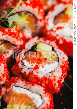Fresh sushi rolls with red fish roe and green vegetables served on a black plate during a food event in a restaurant kitchen setting at lunchtime Fresh sushi rolls with red fish roe and green vegetables served on a black plate during a food event in a restaurant kitchen setting at lunchtime 140651604