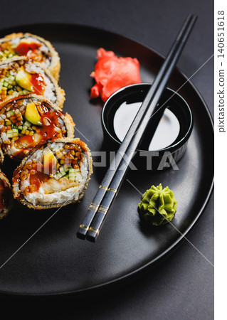 Sushi rolls served on a black plate with chopsticks and garnishes in a dining setting during dinner time Sushi rolls served on a black plate with chopsticks and garnishes in a dining setting during dinner time 140651618