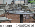 Set upon rich brown, rainwater-slicked wooden decking, this elegant patio features an array of modern bistro tables and curved wicker armchairs with geometric black legs. A softly blurred table in the 140652016