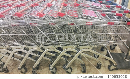Metal shopping trolleys with red handles stacked in a retail store. 140653028