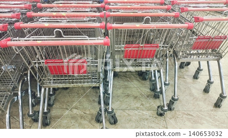 Metal shopping trolleys with red handles stacked in a retail store. 140653032