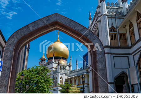 SINGAPORE - JUNE 29, 2025: A low angle view of the majestic golden dome of the Sultan Mosque framed by an Islamic style stone archway in Kampong Glam SINGAPORE - JUNE 29, 2025: A low angle view of the majestic golden dome of the Sultan Mosque framed by an Islamic style stone archway in Kampong Glam 140653309