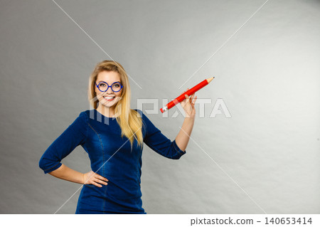 Smiling woman holds big pencil in hand 140653414