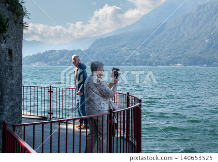 Senior Taking Photos of Lake Como Panorama in Varenna, Italy, During Off-Season Senior Taking Photos of Lake Como Panorama in Varenna, Italy, During Off-Season 140653525