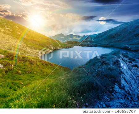 summer solstice scenery of alpine capra lake with steep slopes. day meet night. epic view of transylvania alps. sun and moon in harmony over southern carpathian mountains for astrology wallpaper summer solstice scenery of alpine capra lake with steep slopes. day meet night. epic view of transylvania alps. sun and moon in harmony over southern carpathian mountains for astrology wallpaper 140653707