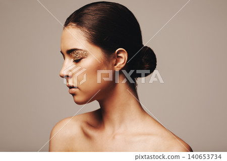 Woman, profile and gold glitter on eyes for beauty, cosmetology and glamour with cosmetics on beige background. Eyeshadow, makeup and fashion model in studio, art or creativity with shimmer and glow Woman, profile and gold glitter on eyes for beauty, cosmetology and glamour with cosmetics on beige background. Eyeshadow, makeup and fashion model in studio, art or creativity with shimmer and glow 140653734
