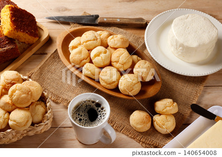 Brazilian breakfast with artisanal cheese bread served on a wooden platter, fresh Minas cheese, black coffee, and cornbread on a rustic table. Brazilian breakfast with artisanal cheese bread served on a wooden platter, fresh Minas cheese, black coffee, and cornbread on a rustic table. 140654008