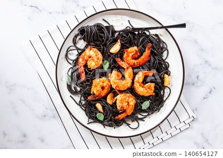 Black spaghetti with shrimp, on a white plate with a fork, on a striped napkin,marble background, homemade, no people, Black spaghetti with shrimp, on a white plate with a fork, on a striped napkin,marble background, homemade, no people, 140654127