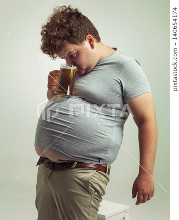 Obese, weight gain and alcohol for man in studio with drink for unhealthy habit, plus size and joke. Overweight person with glass on fat stomach for balance, comedy and humor for lager and comic Obese, weight gain and alcohol for man in studio with drink for unhealthy habit, plus size and joke. Overweight person with glass on fat stomach for balance, comedy and humor for lager and comic 140654174