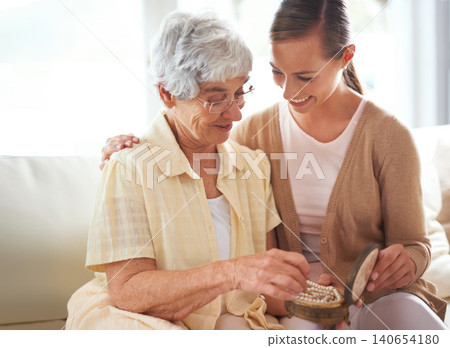 Mother, senior woman and adult daughter with pearl necklace, home and conversation in a living room. Family, pensioner and girl on a couch, relaxing and discussion with jewelry, present and gift Mother, senior woman and adult daughter with pearl necklace, home and conversation in a living room. Family, pensioner and girl on a couch, relaxing and discussion with jewelry, present and gift 140654180