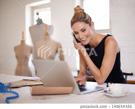 Designer, woman and phone call in boutique for fashion with laptop, communication and excited for deal. Person, smartphone and computer with networking, negotiation and contact for material in studio 140654388