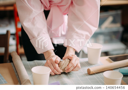 close-up female hands make a clay plate, align the shape with special tools in the workshop close-up female hands make a clay plate, align the shape with special tools in the workshop 140654456