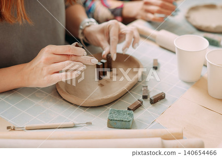 close-up female hands make a clay plate, align the shape with special tools in the workshop close-up female hands make a clay plate, align the shape with special tools in the workshop 140654466
