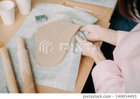close-up female hands make a clay plate, align the shape with special tools in the workshop close-up female hands make a clay plate, align the shape with special tools in the workshop 140654493